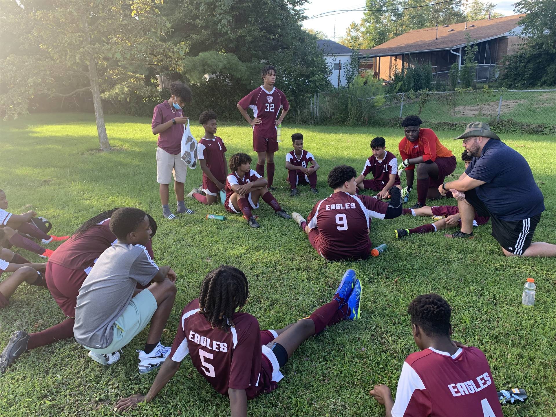 students in soccer uniforms sitting in circle in grass